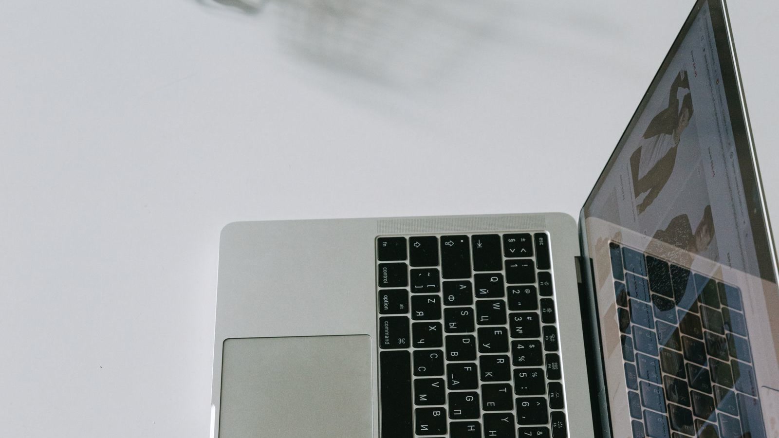 A laptop on a white desk beside a miniature metal shopping trolley, symbolising online shopping and the product data AI shopping agents read before they recommend a retailer.