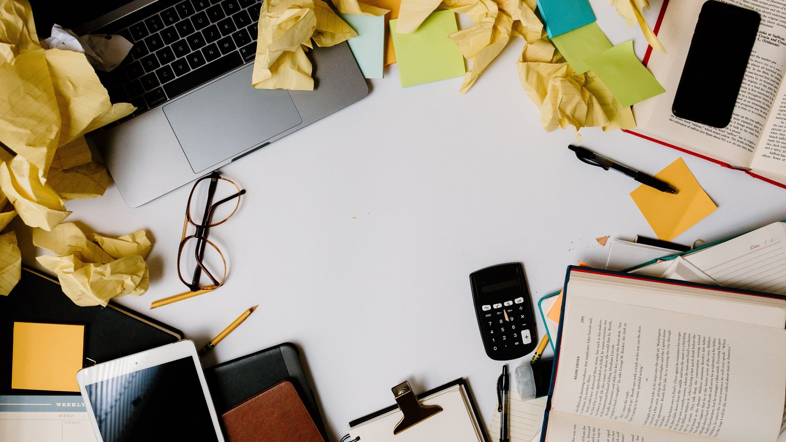 A cluttered desk covered in crumpled notes and sticky notes around a laptop, representing content overload