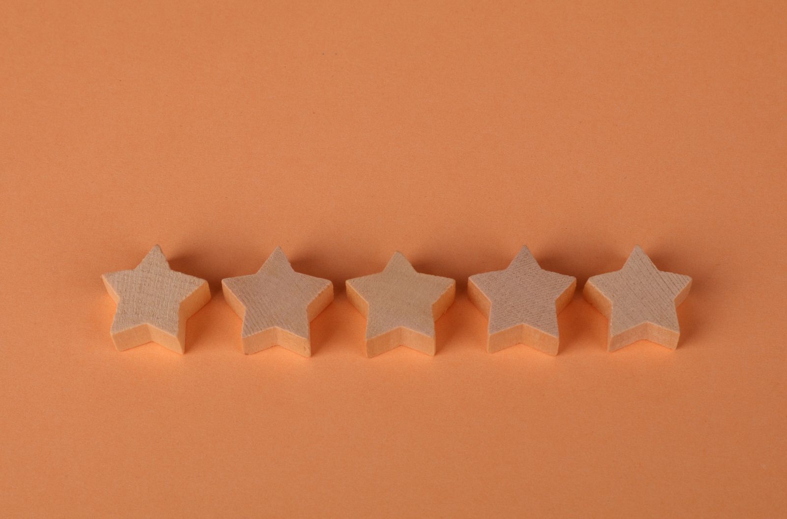 Five wooden star shapes lined up in a row on a plain orange background, representing a five-star customer rating.