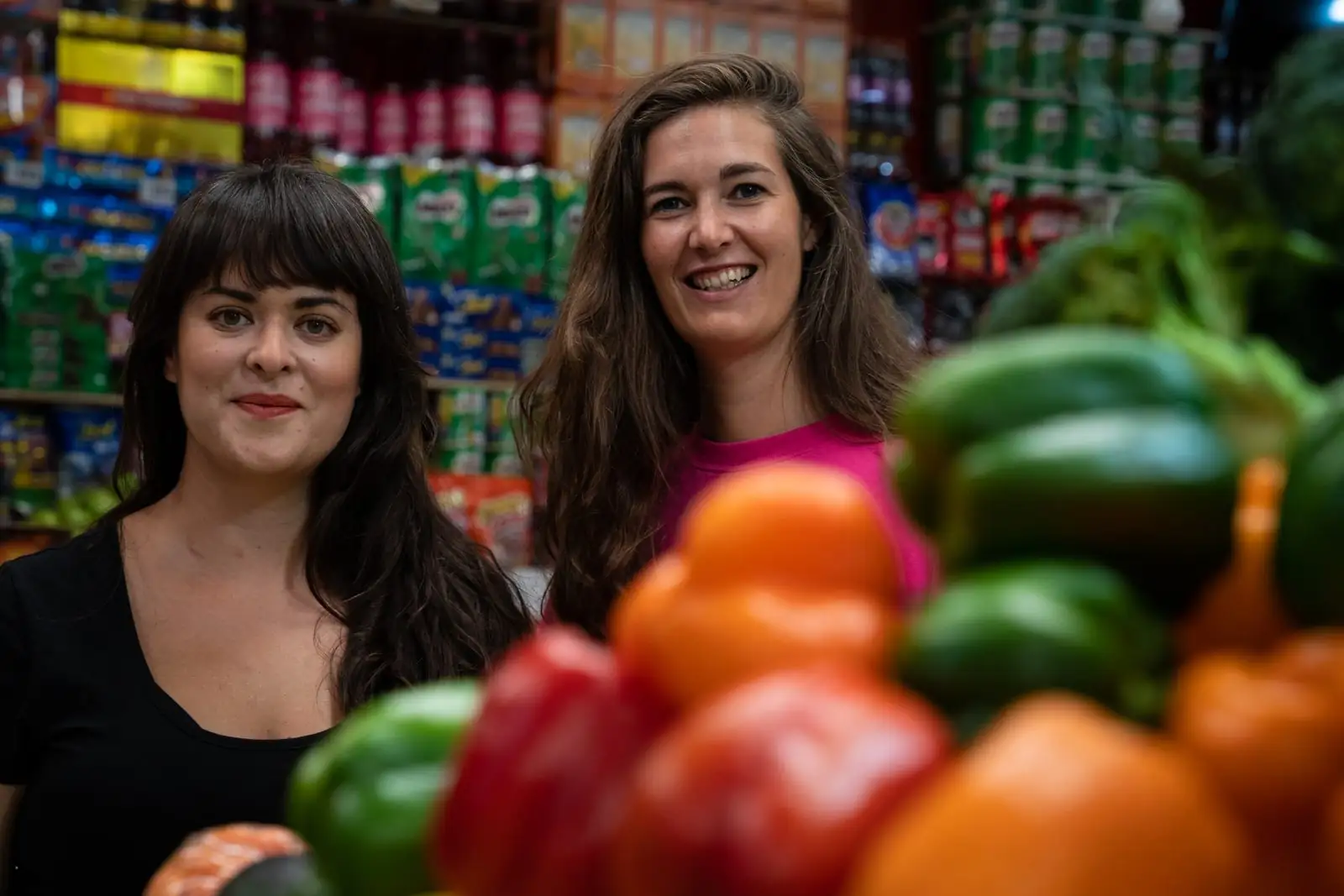 Laura and Andrea from Masafina smiling in a shop aisle behind a display of red and green peppers.