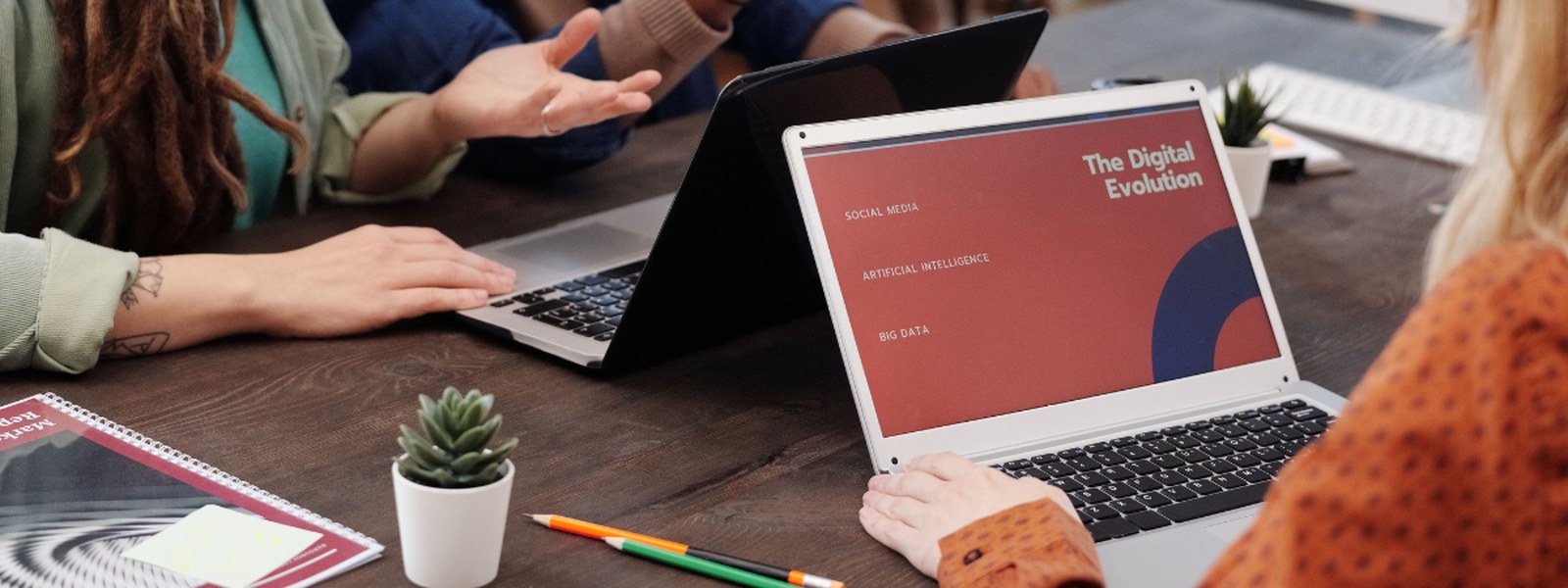 A team meeting around a table with laptops, discussing a presentation