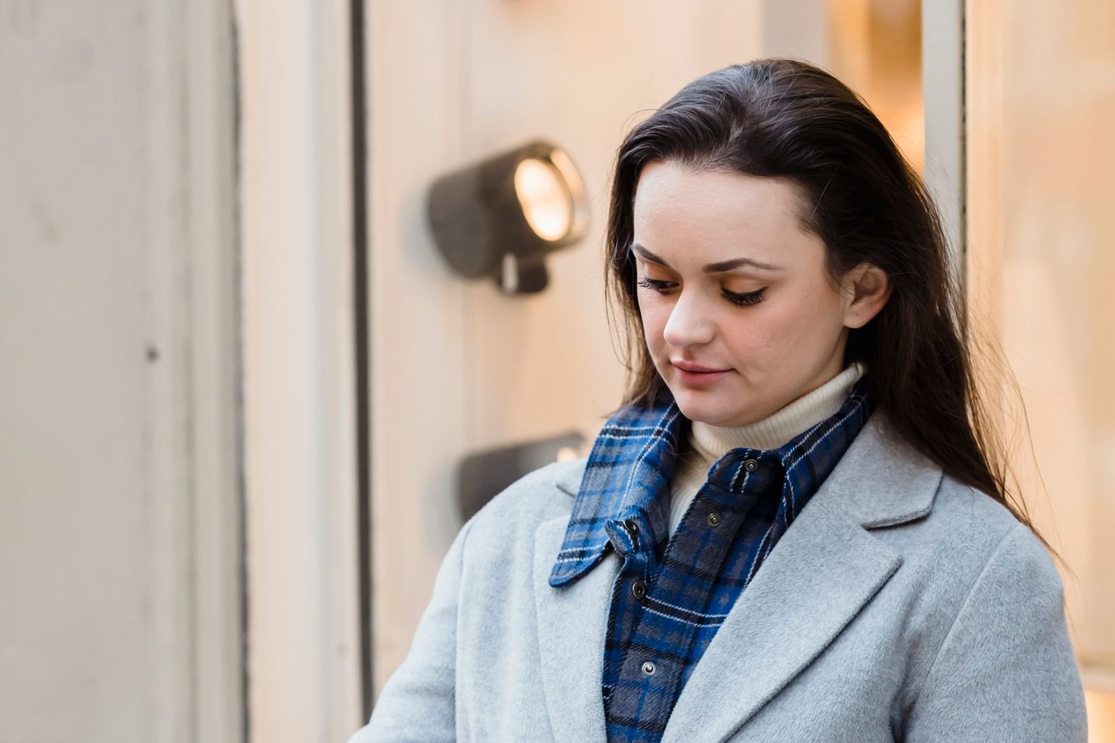 Woman in a grey coat holding shopping bags and checking her smartphone outside a shop window, representing a local shopper searching for deals.