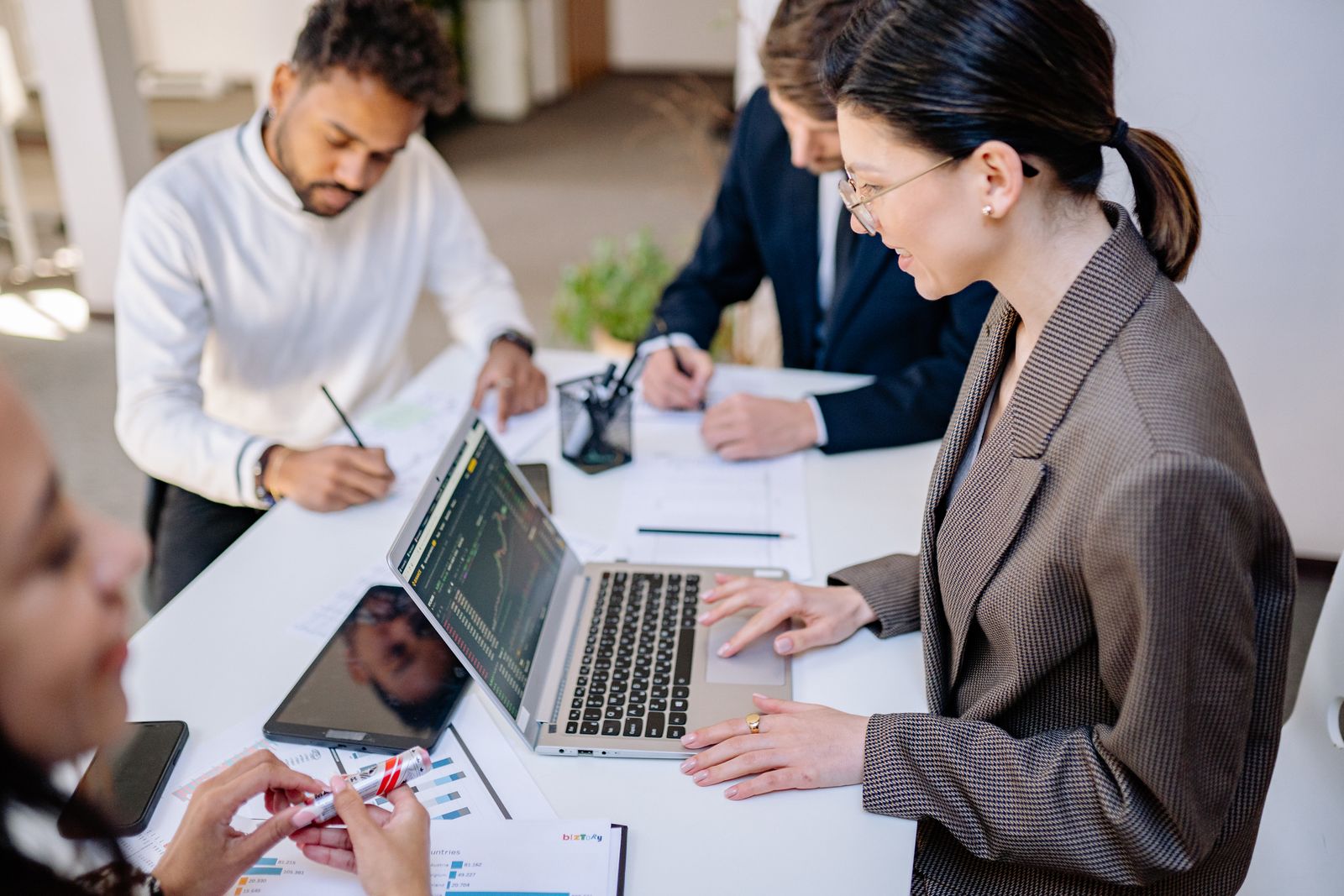 A business team around a white table reviewing charts on a laptop and tablet during a planning meeting, representing an agency and client reviewing Google Ads performance by network.