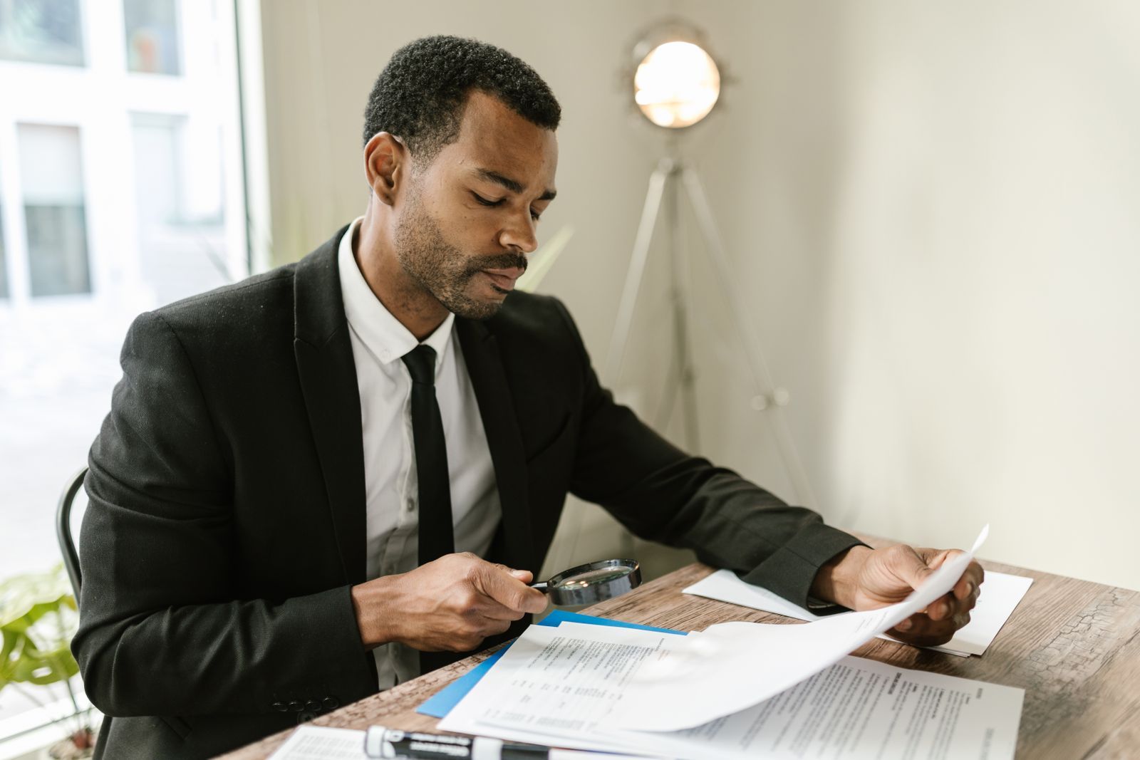 A man in a dark suit studying a printed report through a magnifying glass at his desk, the level of scrutiny SEO ranking reports need before anyone acts on a sudden drop.