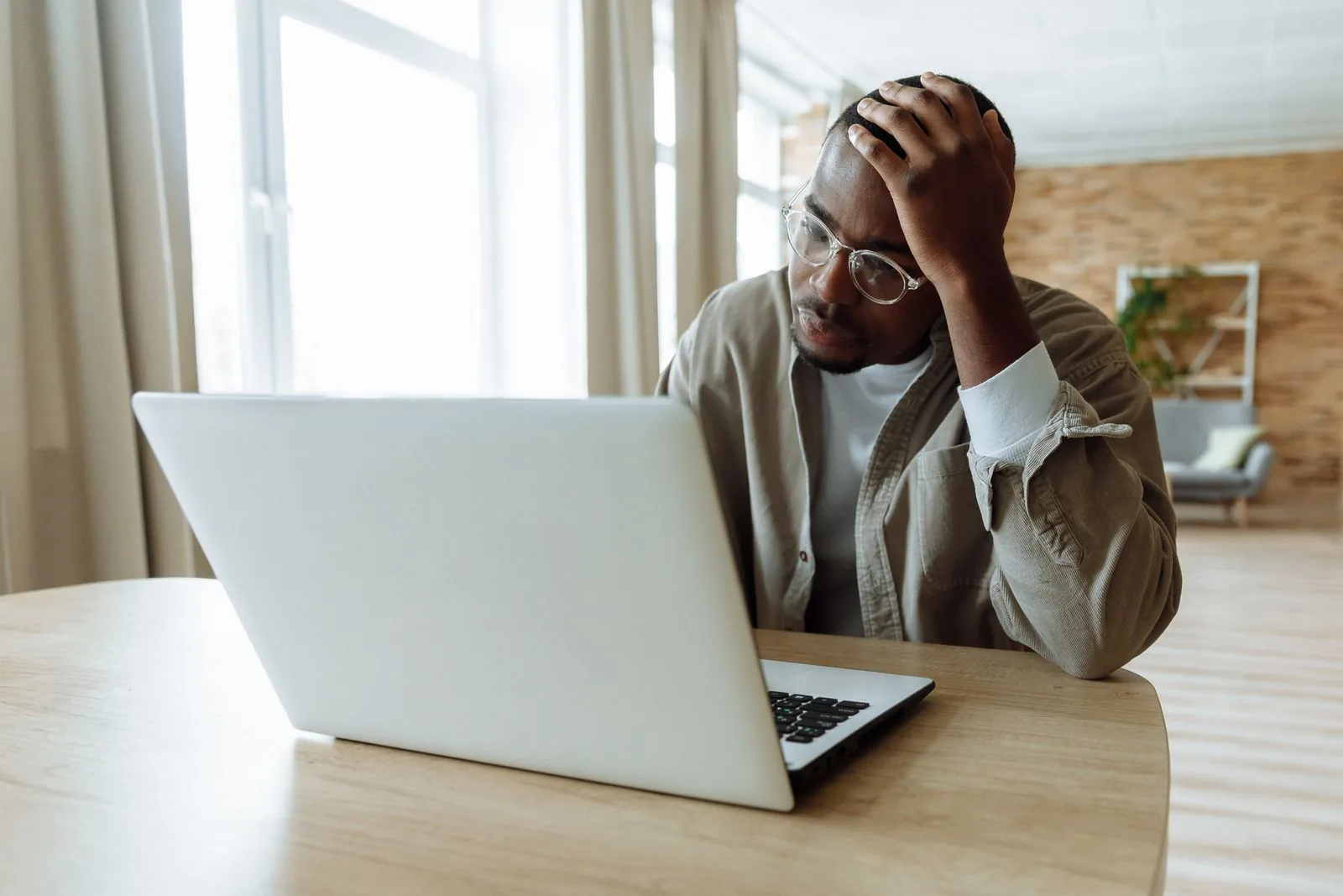 A man in glasses with his hand on his head, staring at a laptop at a wooden desk, representing a UK business owner who has just seen Google rankings drop after the September 2026 spam update.