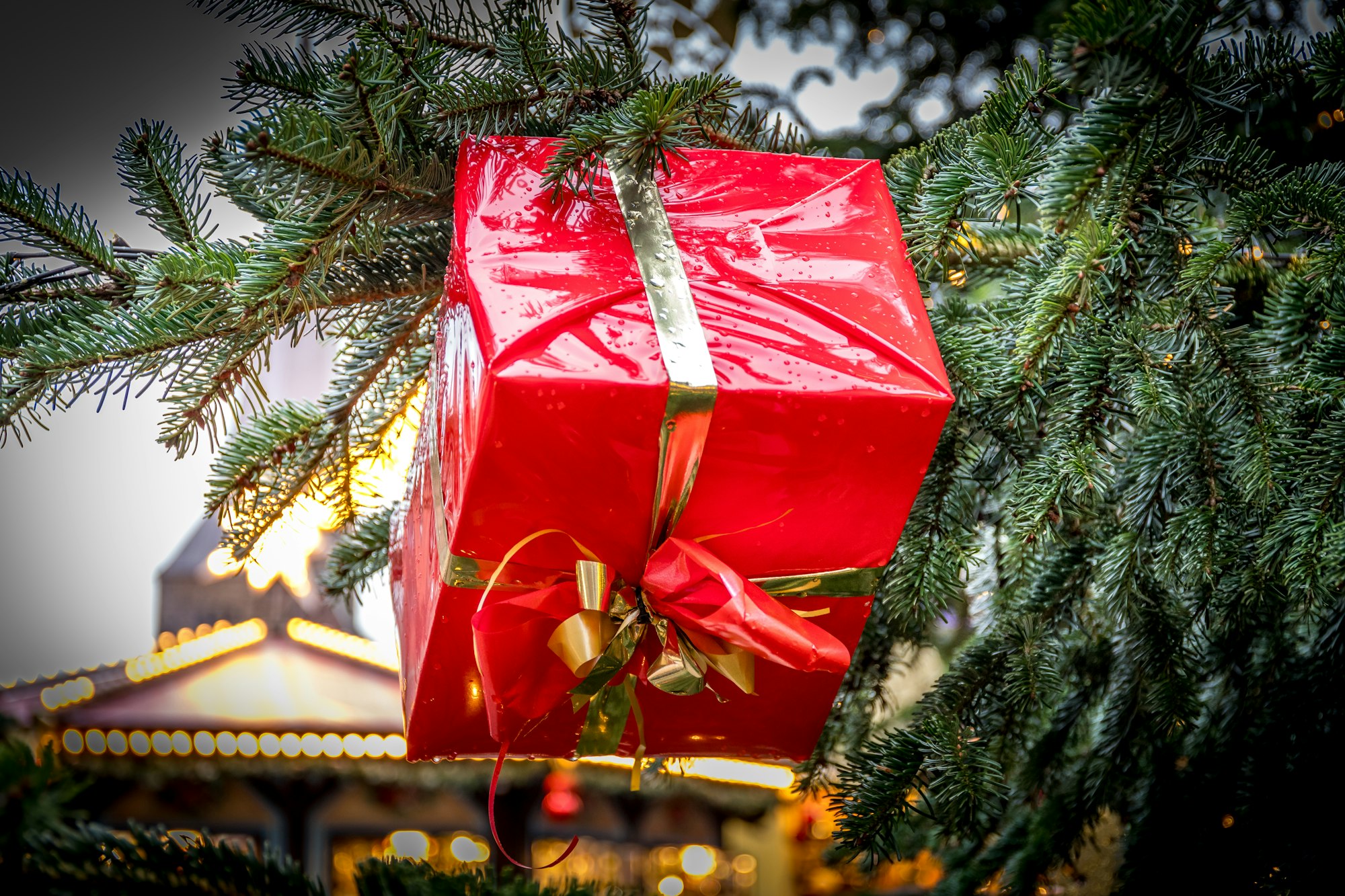 A red gift box tied with red and gold ribbon hanging on a Christmas tree, standing in for the gift-giving idea behind the John Lewis Christmas advert.