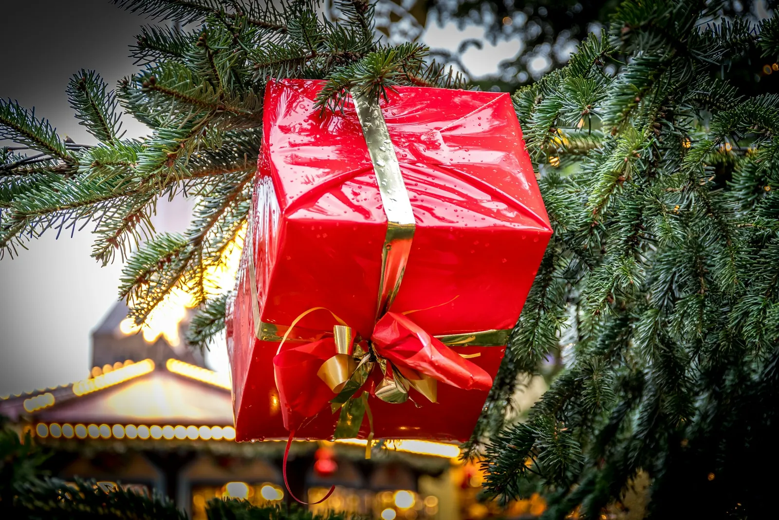 A red gift box tied with red and gold ribbon hanging on a Christmas tree, standing in for the gift-giving idea behind the John Lewis Christmas advert.