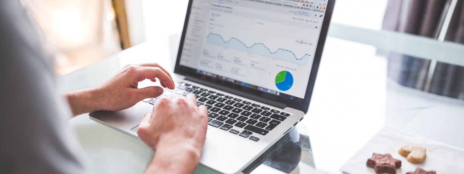 Hands typing on a laptop showing an analytics dashboard with a line chart and pie chart