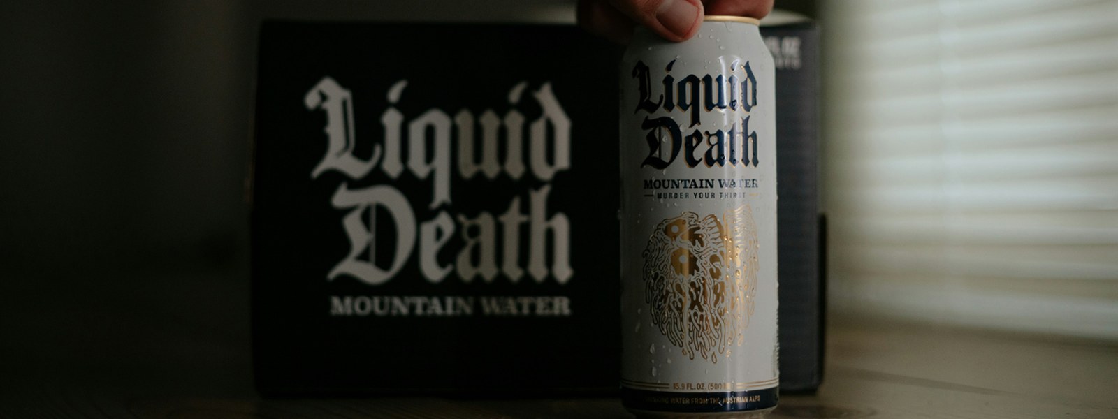A can of Liquid Death Mountain Water held in front of its branded box packaging