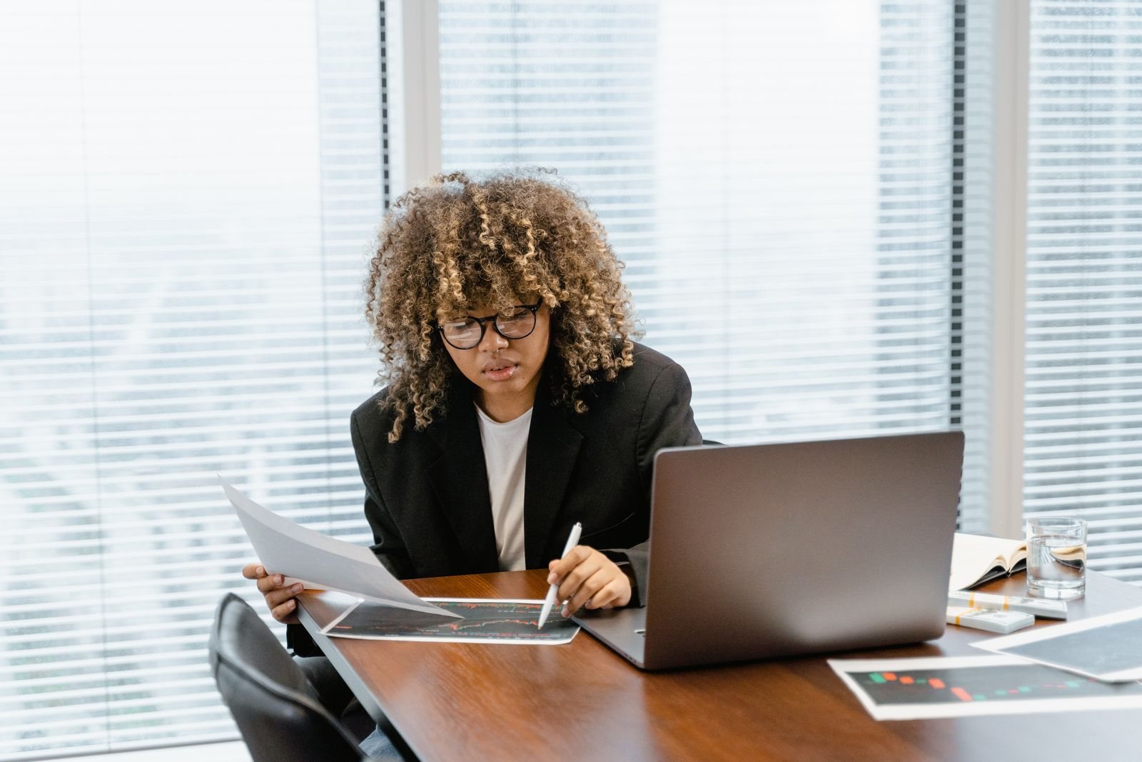 A woman at an office desk reviewing printed charts beside a laptop, representing an advertiser comparing Meta Ads Manager results with their own analytics after 28 October.