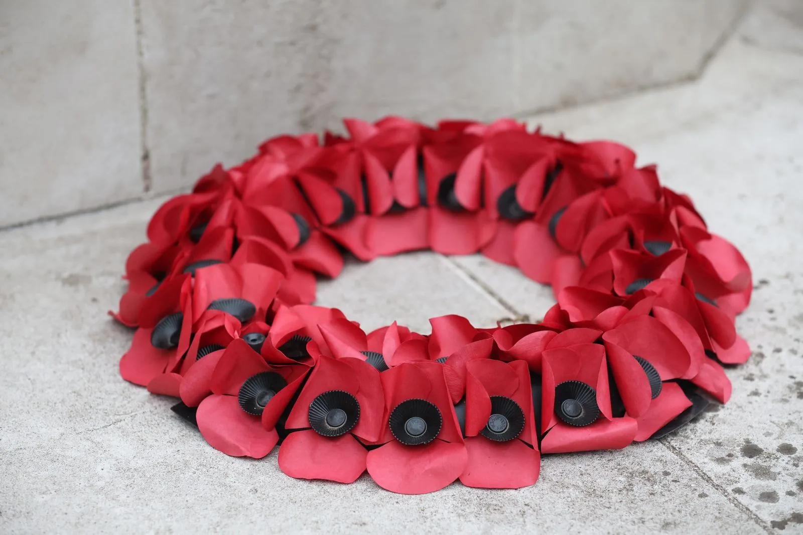 A red paper poppy wreath laid on a stone surface, the symbol of the Royal British Legion, which partnered with Sainsbury's on the 1914 Christmas truce advert.