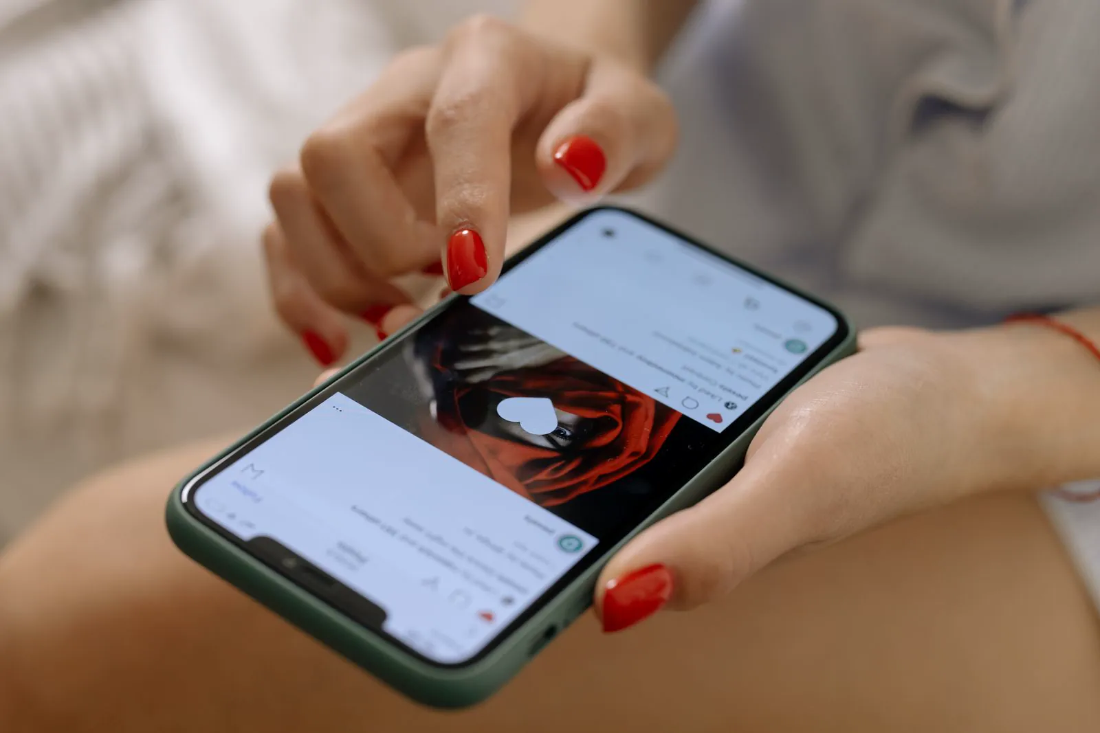 Close-up of a woman's hands with red nails scrolling a social media feed on a smartphone, representing a UK consumer seeing ads in the Threads feed.