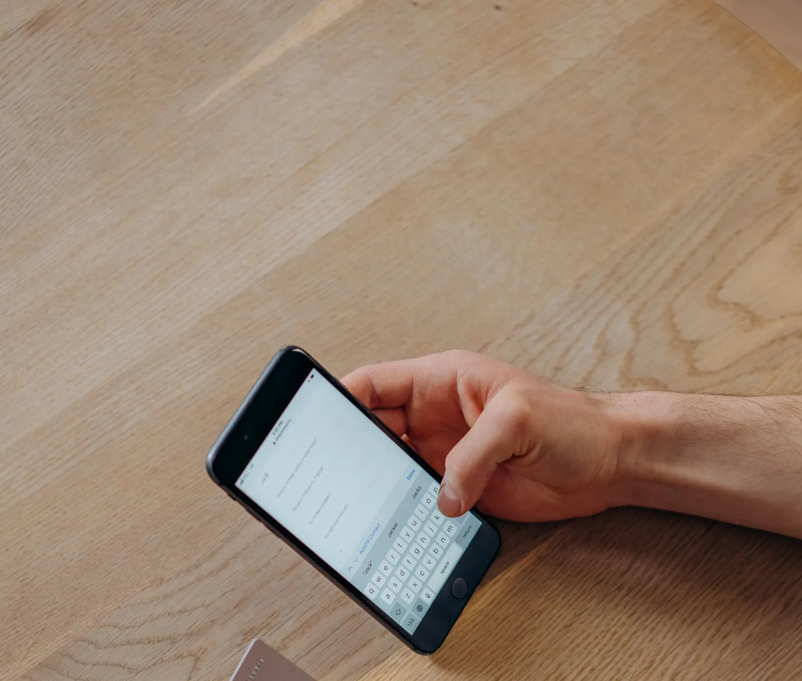 A person holding a smartphone in one hand and a bank card in the other at a wooden table, the moment of purchase that TikTok Shop Net Sales Boost charges an ad fee against.