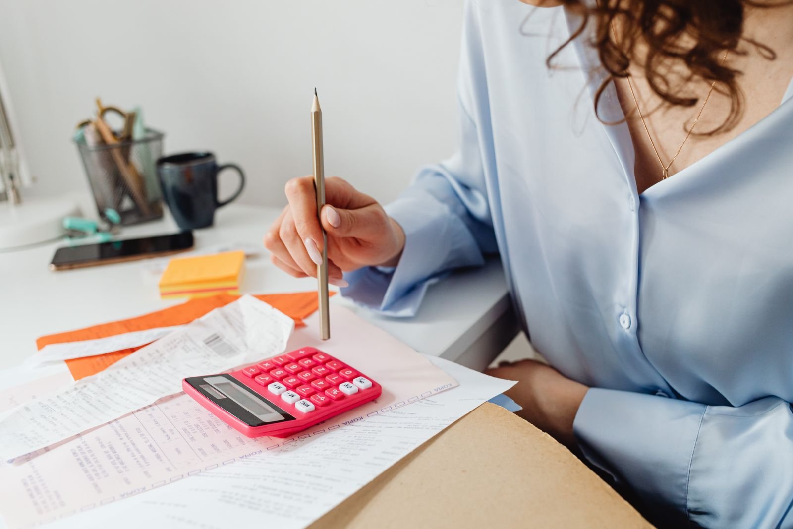 A woman with a pencil working out figures on a pink calculator over printed papers at her desk, the kind of maths UK UGC creators should do before sending a rate card.
