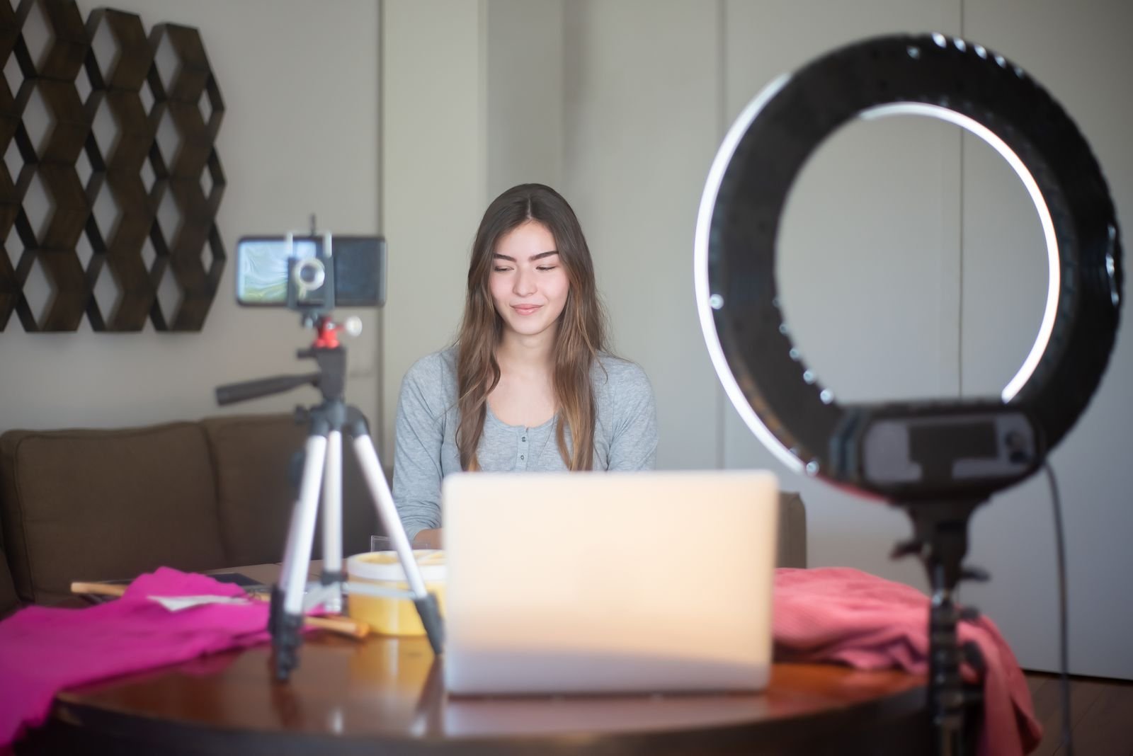 A creator sitting at a table in a home studio with a smartphone on a tripod, a ring light and a laptop, getting ready to film a UGC video for a brand brief.